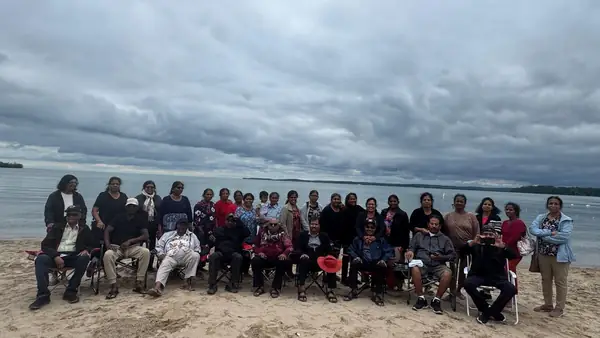 People seated together on a beach by the water under a cloudy sky