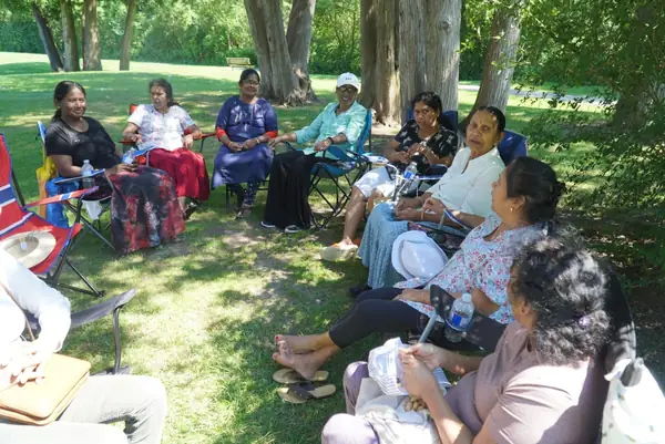 People seated in a circle of lawn chairs under trees