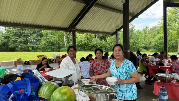 People gathered at a picnic table with fruit under a pavilion