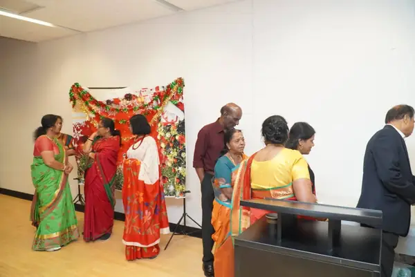 Women in saris and men gathered by a decorated display indoors