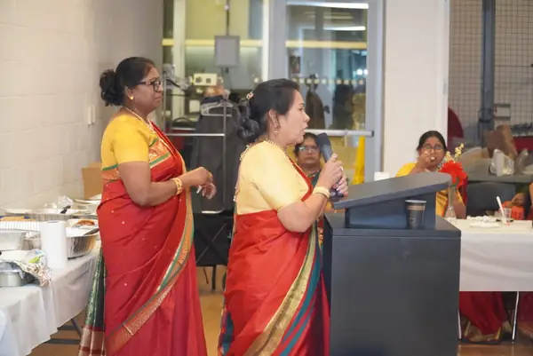 Two women in saris speaking into a microphone
