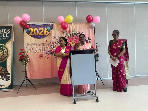 Two women at a podium beside a 2026 backdrop with balloons