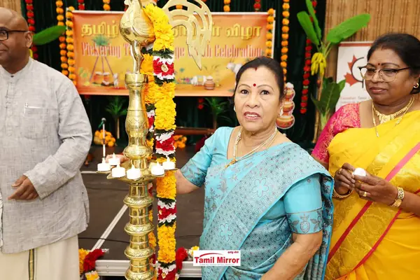 Two women beside a traditional brass lamp in front of a banner